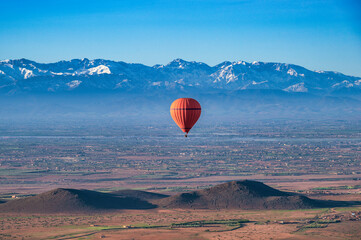 A red, hot air balloon, floating over the desert near Marrakech, Morocco on a  clear spring day, with the snow capped Atlas mountains in the background