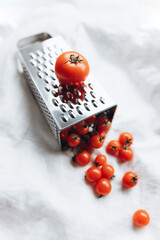 Grater with a tomato on it with cherry tomatoes on a white background 