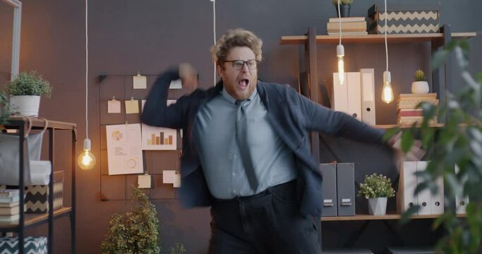 Loop portrait of creative office worker dancing and screaming listening to music having fun enjoying break at work in evening. People and workplace concept.
