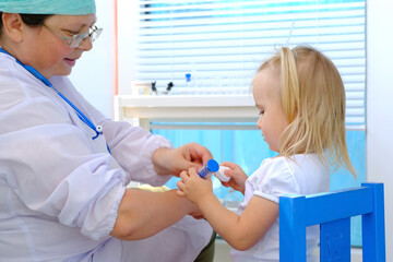 female doctor, pediatrician examines small child, 2-year-old girl with white hair, vaccinates,...