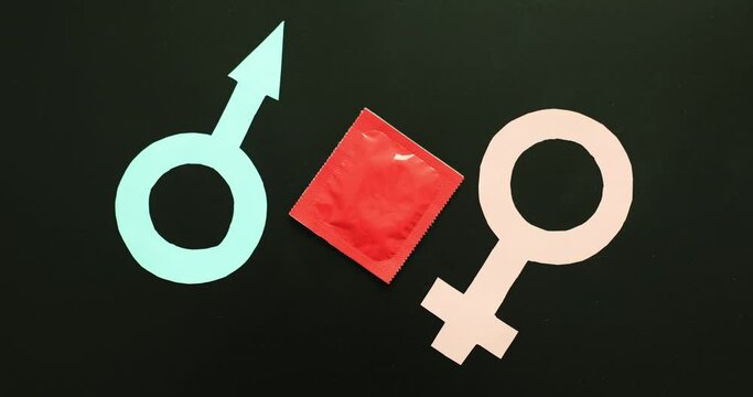 Hand of woman putting condom in red package between male and female symbols on black background. Intimate relationship between man and woman