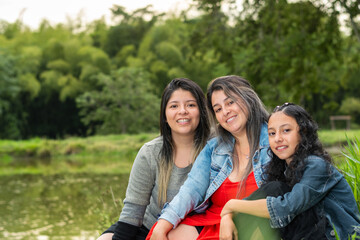 three latina girls sitting together on the lawn by the fishing lake