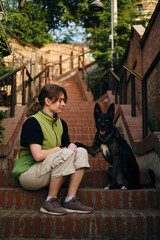Charming black doggy sits on old brick staircase and poses with young female owner. Old town Zemun,...