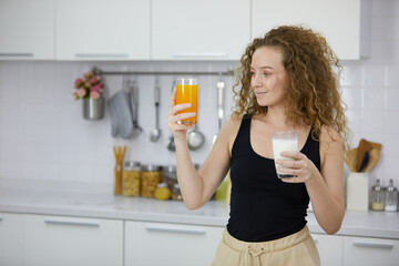 young woman holding orange juice and milk in the kitchen