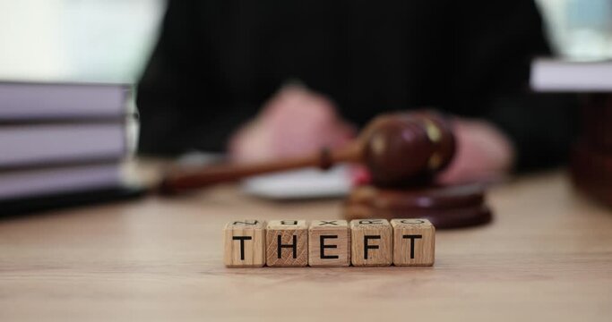 Word Theft made of wooden cubes against judge writing down verdict on paper. Trial and sentence for taking possession of property. Gavel and law books on table