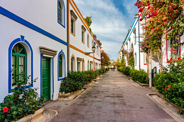 Fototapeta premium Street with blooming flowers in Puerto de Mogan, Gran Canaria, Spain. Favorite vacation place for tourists and locals on island. Puerto de Mogan with lots of bougainvillea flowers, Canary Island.