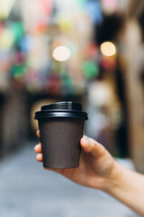 Woman gives paper black coffee cup or tea on urban background. Take away or delivery concept. Copy...