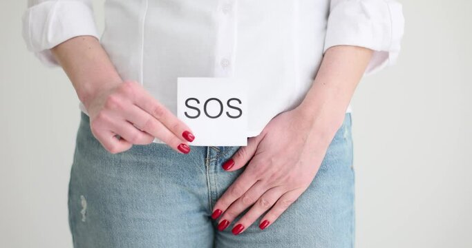 Female covers groin with hand and shows message SOS in light office. Woman suffers from strong pain in genital area. Symptoms of gynecological disease slow motion
