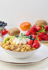 Granola with strawberries, kiwi, banana and blueberries in a round plate topped with yogurt on the table.
