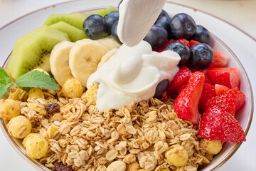 Granola with strawberries, kiwi, banana and blueberries in a round plate topped with yogurt on the...