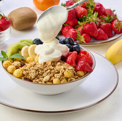Granola with strawberries, kiwi, banana and blueberries in a round plate on a white table. Healthy and tasty food