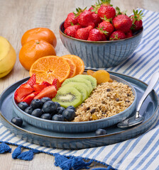 Granola with strawberries, kiwi, banana and blueberries in a round plate on a white table.