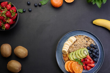 Granola with strawberries, kiwi, banana and blueberries in a round plate on a black table. Healthy...