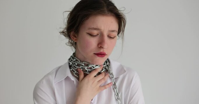 Upset woman suffers from sore throat comparing with metal chains around neck. Throat contraction concept. Female person touches ill body part slow motion