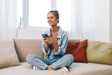 Obraz premium Smiling woman holding mobile phone while relaxing on a cozy sofa in a modern living room