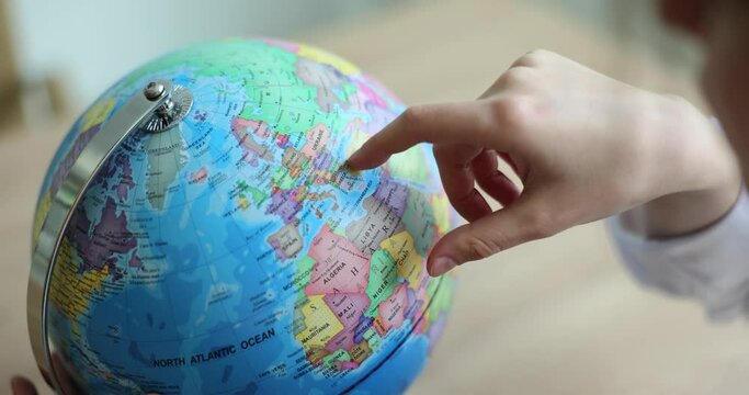 Schoolchild swipes finger over countries on globe in premise. Student studies Earth surface while gaining knowledge at school and dreams about travel abroad slow motion