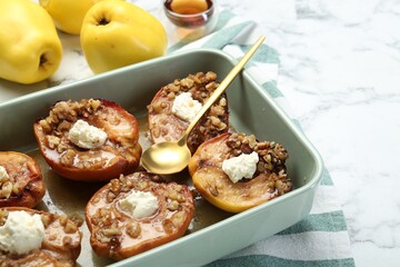Tasty baked quinces with nuts and cream cheese in dish on white marble table, closeup. Space for...