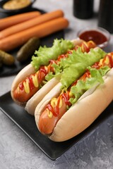 Tasty hot dogs with lettuce, ketchup and mustard on grey textured table, closeup