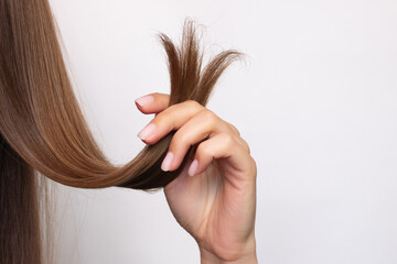 A woman holds in her hand a strand of hair with damaged, dry, split ends, close-up. Isolated on a...