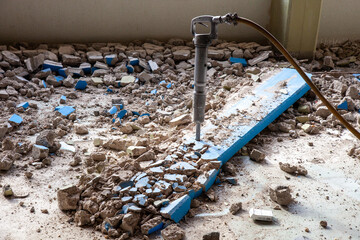 A pneumatic jackhammer demolishes walls and floor, creating a cloud of dust and debris. The...