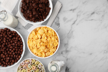 Different delicious breakfast cereals and milk on white marble table, flat lay. Space for text