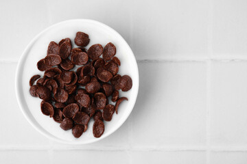 Breakfast cereal. Chocolate corn flakes and milk in bowl on white tiled table, top view. Space for text