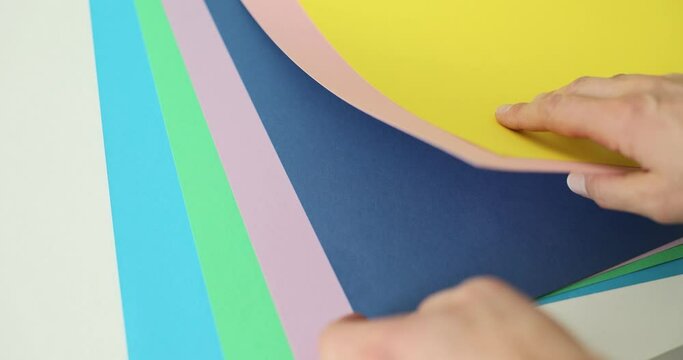 Interior designer examines sheets with color gamut samples for stylish apartment renovation. Hands of woman with colorful papers over white table