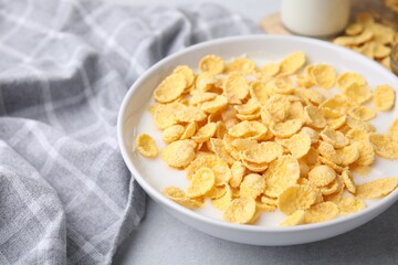 Breakfast cereal. Corn flakes and milk in bowl on light grey table, closeup