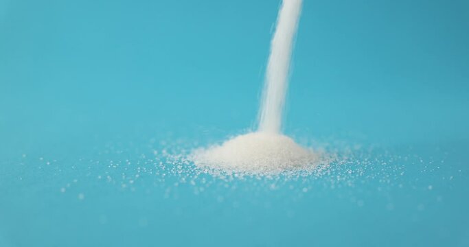 White sugar crystals poured in heap on blue background. Sweet-tasting food product. Carbohydrate additive to meals made from sugar beet