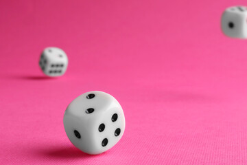 Many white game dices falling on pink background, closeup
