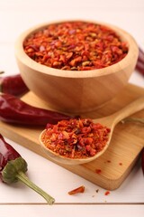 Chili pepper flakes and pods on white wooden table, closeup