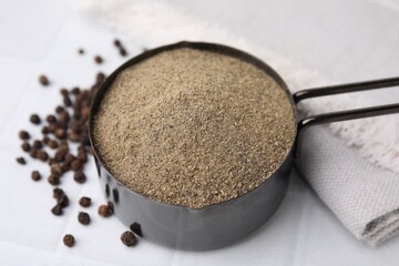 Ground pepper and peppercorns on white tiled table, closeup