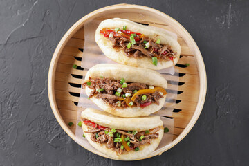 Delicious gua bao in bamboo steamer on black table, top view