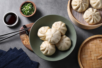 Delicious bao buns (baozi), chopsticks, soy sauce and green onion on grey table, flat lay
