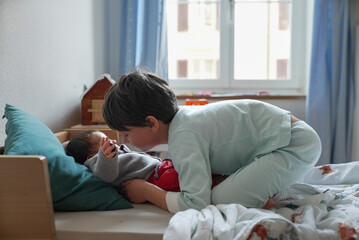 Older sibling tenderly leaning towards newborn baby on the bed, creating a sweet moment of sibling...