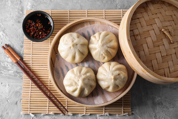 Delicious bao buns (baozi), chopsticks and sauce on grey textured table, flat lay