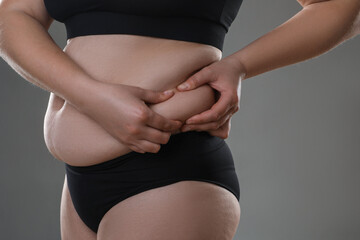 Woman touching belly fat on grey background, closeup. Overweight problem