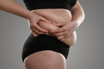 Woman touching belly fat on grey background, closeup. Overweight problem