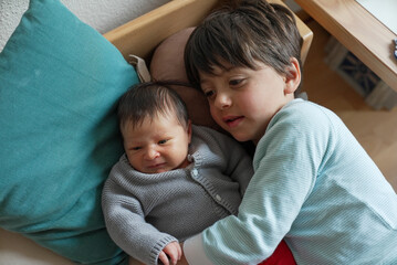 Older sibling cuddling with newborn baby, both nestled on soft pillows. The cozy and intimate...
