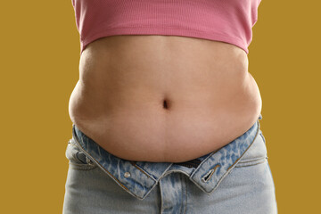 Woman with excessive belly fat on goldenrod background, closeup. Overweight problem