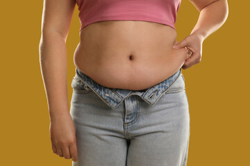 Woman touching belly fat on goldenrod background, closeup. Overweight problem