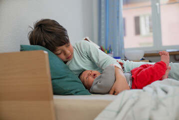 Older sibling lying down with newborn baby, both resting peacefully. The room’s soft lighting and...