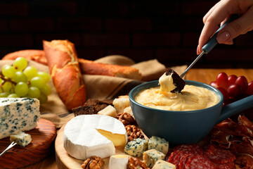 Woman dipping piece of bread into fondue pot with melted cheese at table, closeup