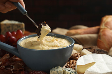 Woman dipping piece of bread into fondue pot with melted cheese at table, closeup