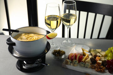 Fork with piece of apple, melted cheese in fondue pot, wine and products on grey table