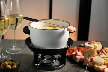 Forks with pieces of ham, bread and fondue pot with melted cheese on grey table, closeup