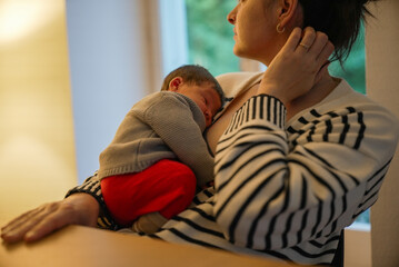 Mother cradling newborn baby in her arms, both dressed warmly, as they share a serene moment...