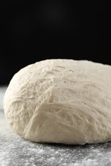 Raw homemade dough and flour on black table, closeup