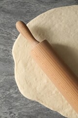 Raw dough and rolling pin on grey table, top view