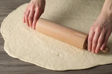 Woman rolling raw dough at wooden table, closeup